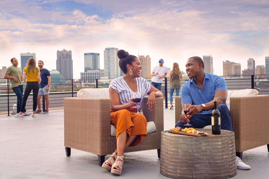 a man and a woman sit on rattan chairs on a roof top with a view of